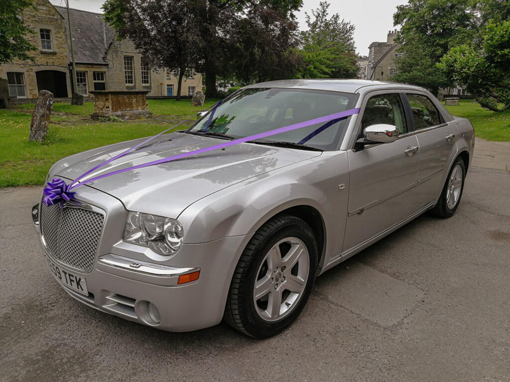 Silver Chrysler 300c parked in the grounds of a church yard for a wedding ceremony