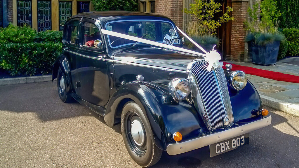 Black Standard Flying 12 with white ribbons parked outside a wedding venue