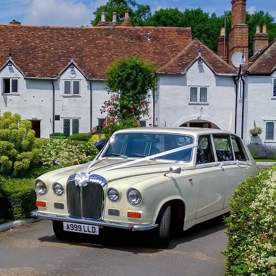 Ivory Classic Daimler DS420 Limousine decorated with white ribbons arriving at a wedding venue